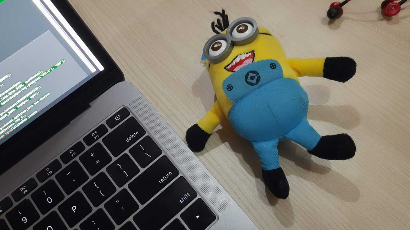 Laptop on a desk with some code open, and a minion stuffed toy next to it.